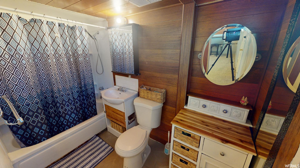 Full bathroom featuring toilet, wood walls, shower / bath combination with curtain, and large vanity