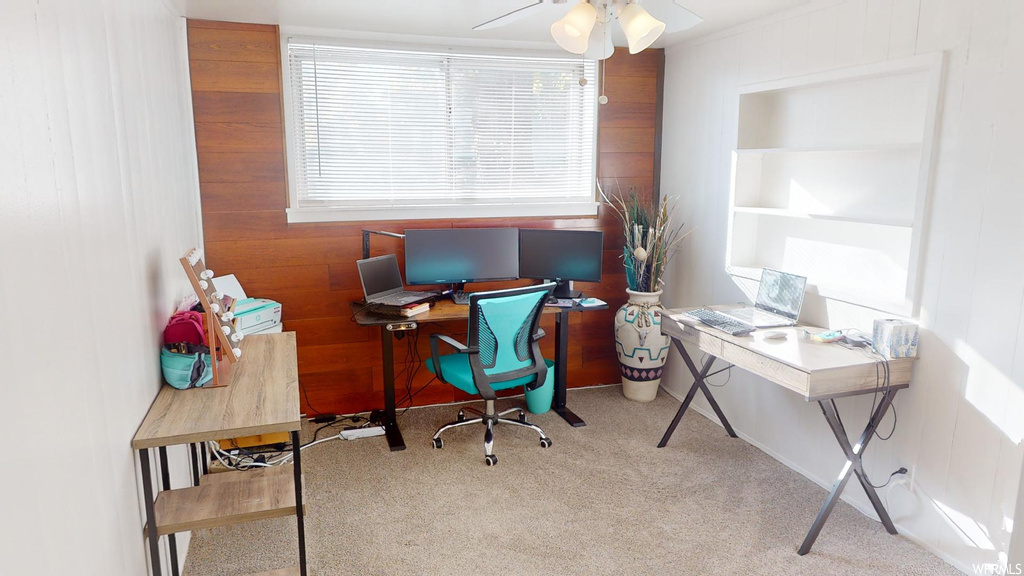 Carpeted home office featuring wood walls and ceiling fan