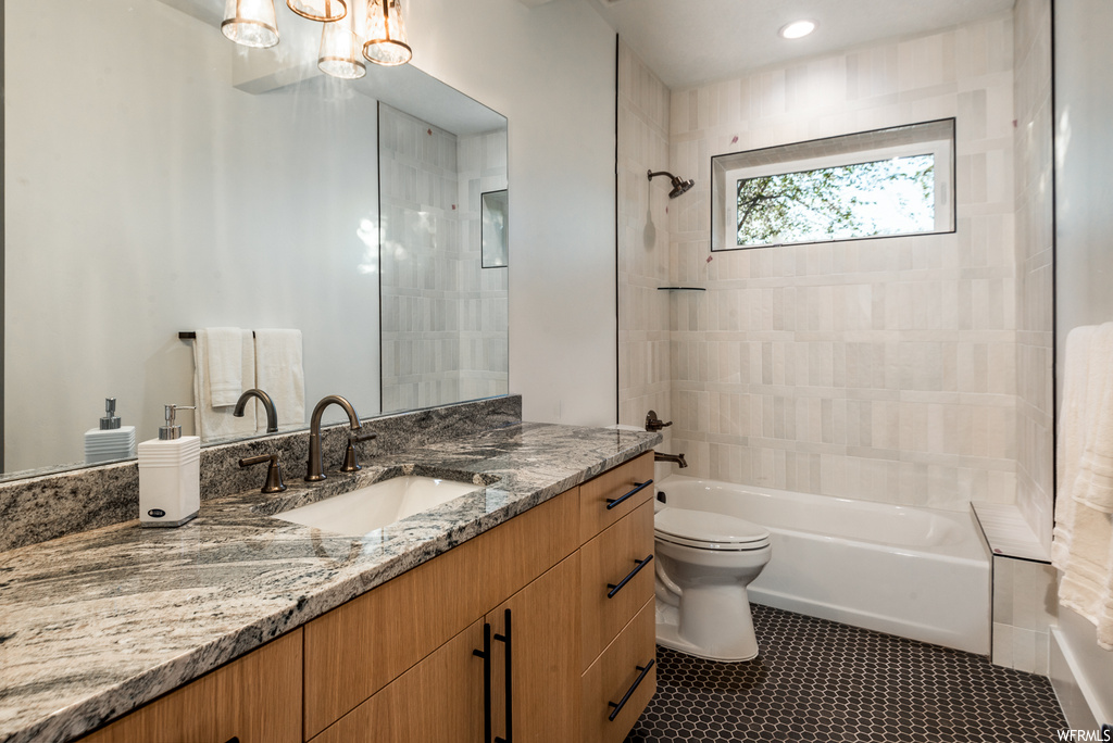 Full bathroom with toilet, tiled shower / bath, oversized vanity, tile flooring, and a notable chandelier