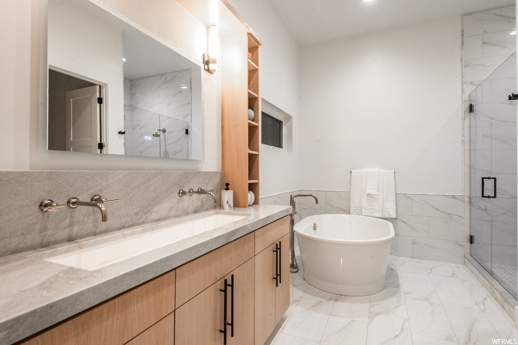 Bathroom featuring tile walls, large vanity, tile floors, dual sinks, and separate shower and tub
