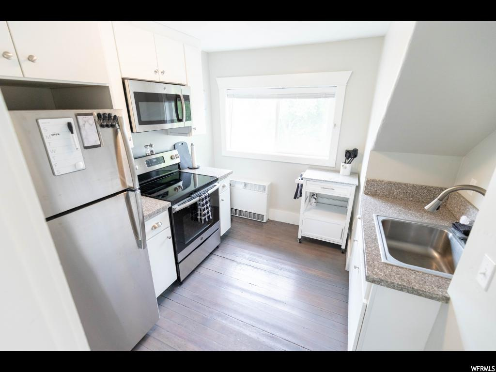 Kitchen with radiator, white cabinets, hardwood floors, stainless steel appliances, and sink