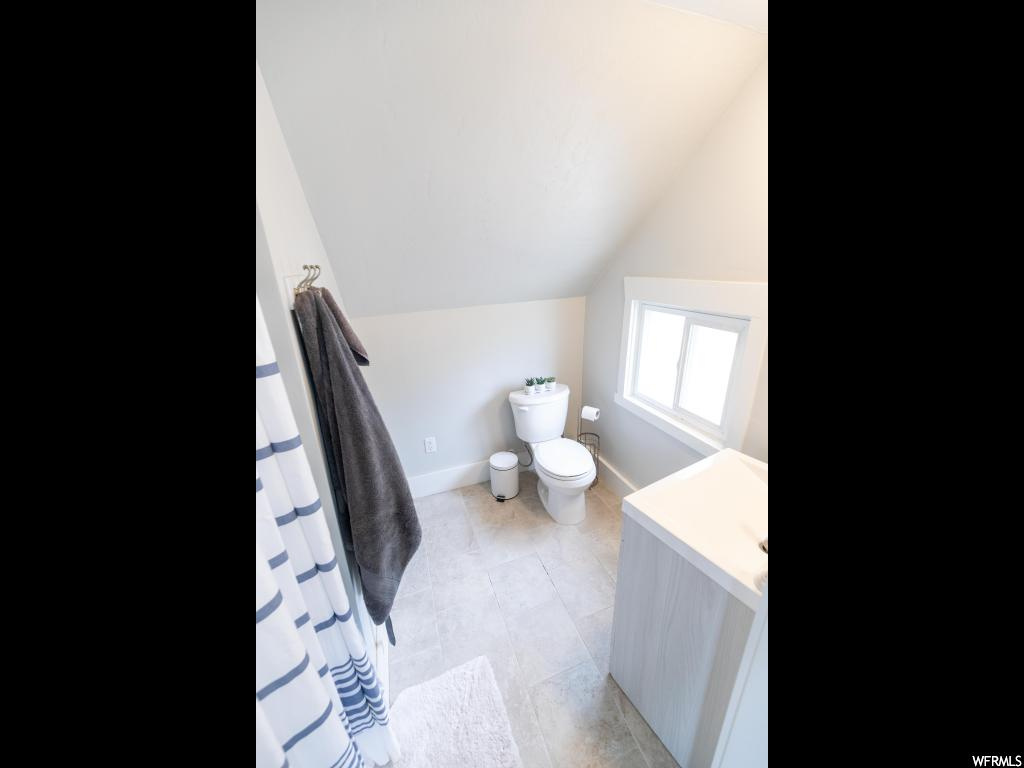 Bathroom with lofted ceiling, vanity, tile flooring, and toilet