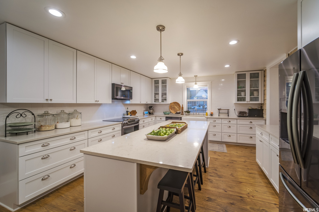 Kitchen with a kitchen island, white cabinetry, appliances with stainless steel finishes, hardwood floors, and decorative light fixtures
