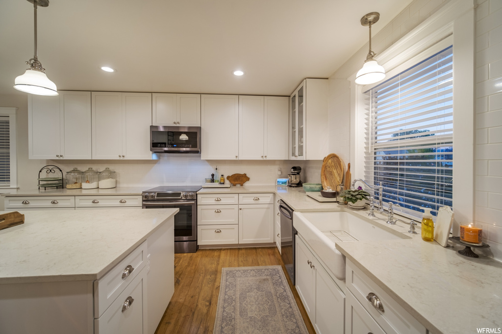Kitchen featuring white cabinetry, stainless steel appliances, decorative light fixtures, and light hardwood flooring