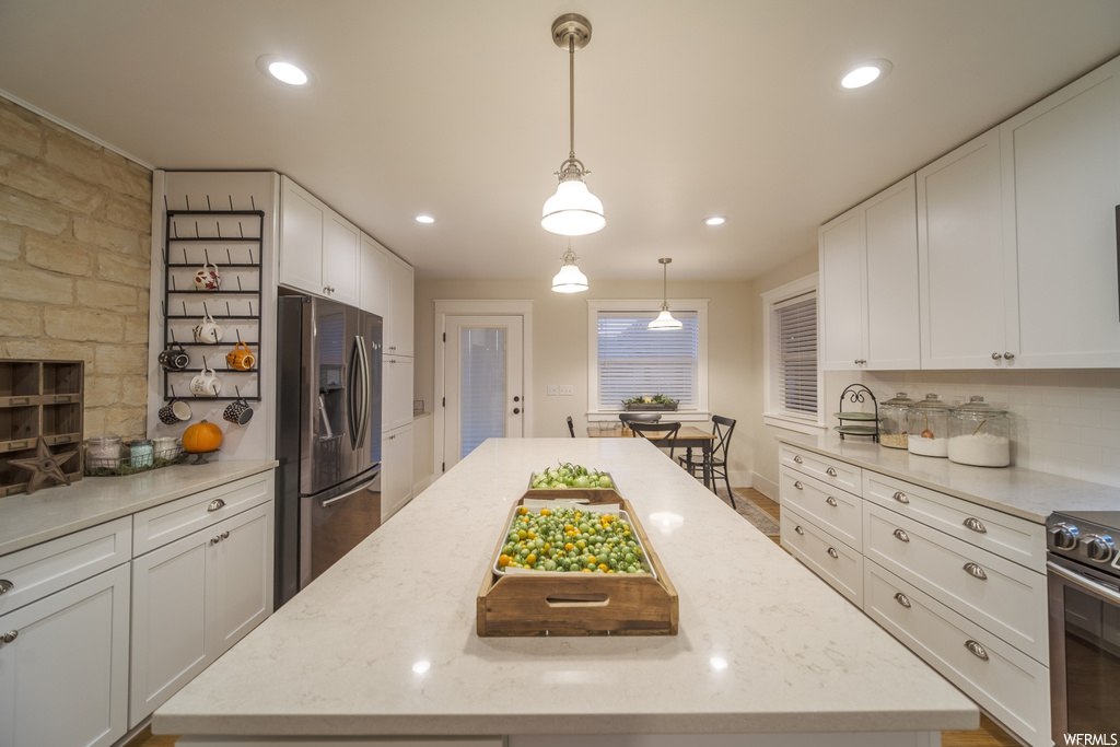 Kitchen with white cabinets, stainless steel refrigerator with ice dispenser, a center island, and decorative light fixtures