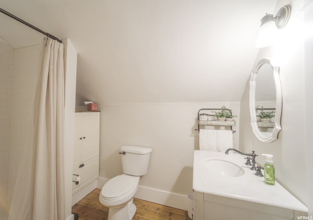 Bathroom with toilet, hardwood flooring, vaulted ceiling, and vanity