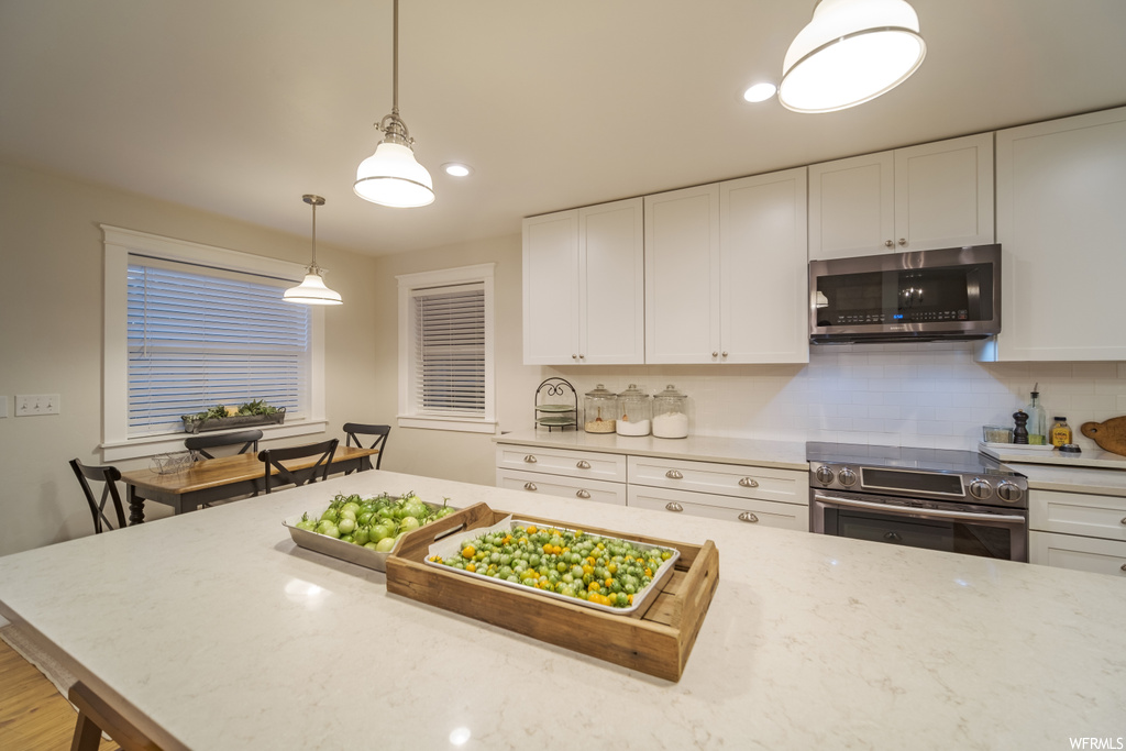 Kitchen featuring pendant lighting, backsplash, white cabinets, and appliances with stainless steel finishes