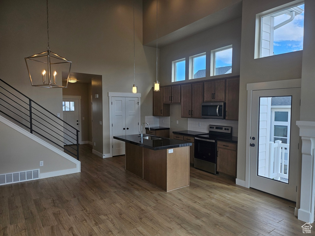 Kitchen with stainless steel appliances, a kitchen island with sink, hardwood / wood-style flooring, a notable chandelier, and tasteful backsplash