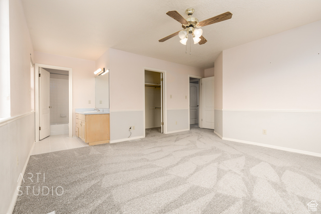Unfurnished bedroom featuring a spacious closet, ceiling fan, a closet, ensuite bathroom, and light colored carpet