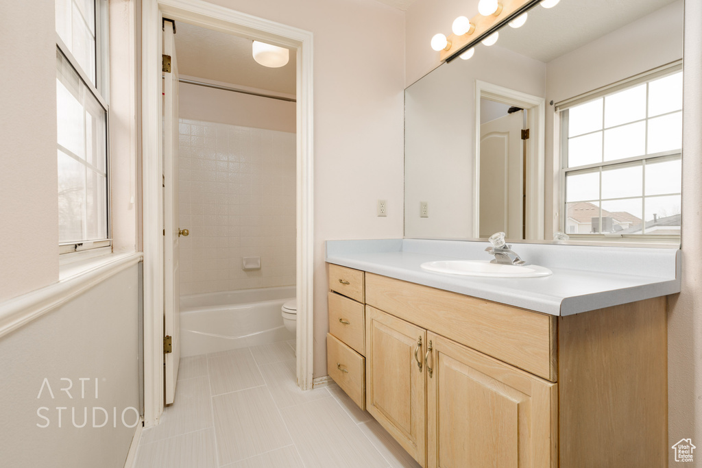 Full bathroom with tiled shower / bath, tile flooring, oversized vanity, and toilet