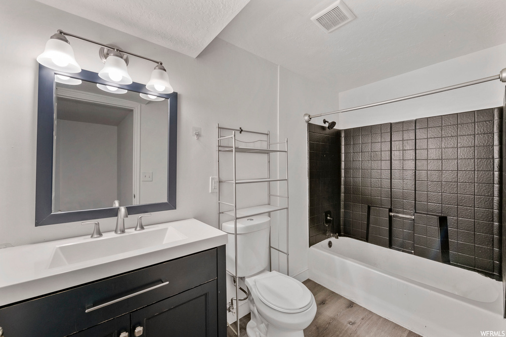 Full bathroom with toilet, a textured ceiling, large vanity, tiled shower / bath combo, and wood-type flooring