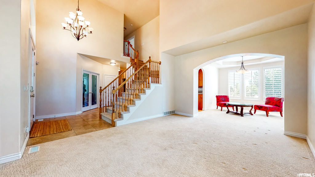 Carpeted foyer featuring a high ceiling, a chandelier, and a raised ceiling