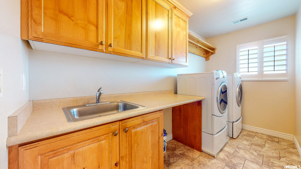 Laundry area featuring sink, cabinets, light tile floors, and washer and clothes dryer