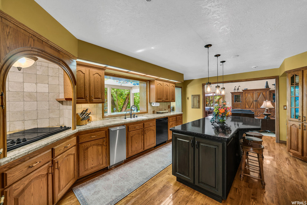 Kitchen featuring backsplash, a center island, light hardwood flooring, dark stone countertops, and decorative light fixtures