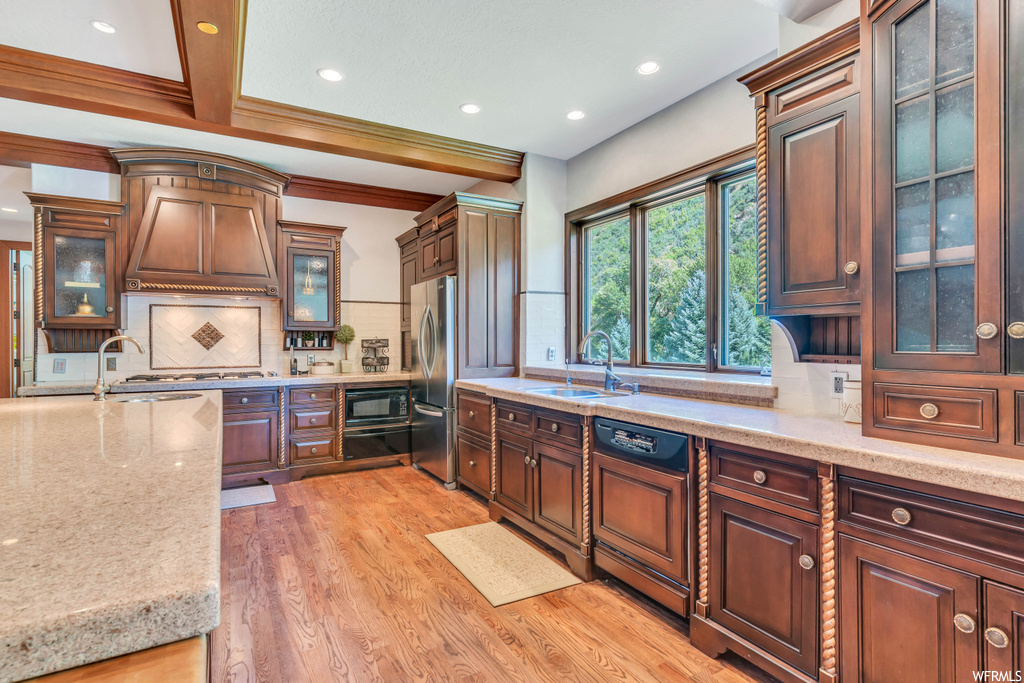 Kitchen featuring light hardwood floors, custom exhaust hood, backsplash, sink, and beamed ceiling