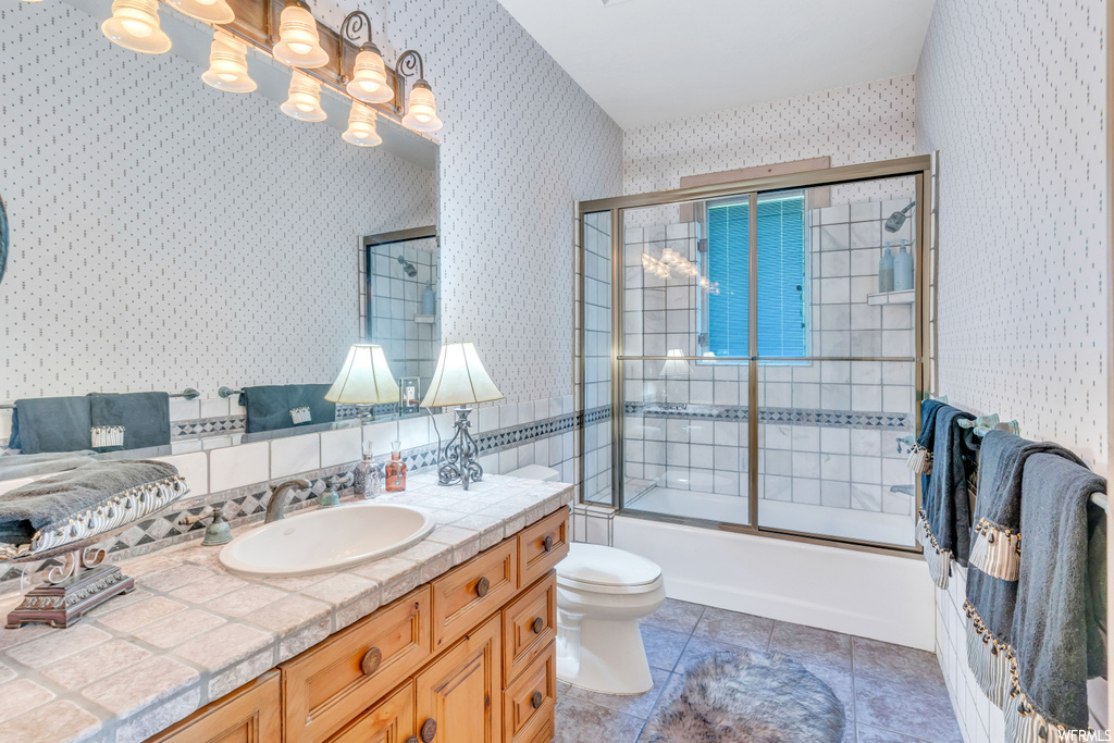 Full bathroom featuring shower / bath combination with glass door, toilet, vanity, and tile flooring