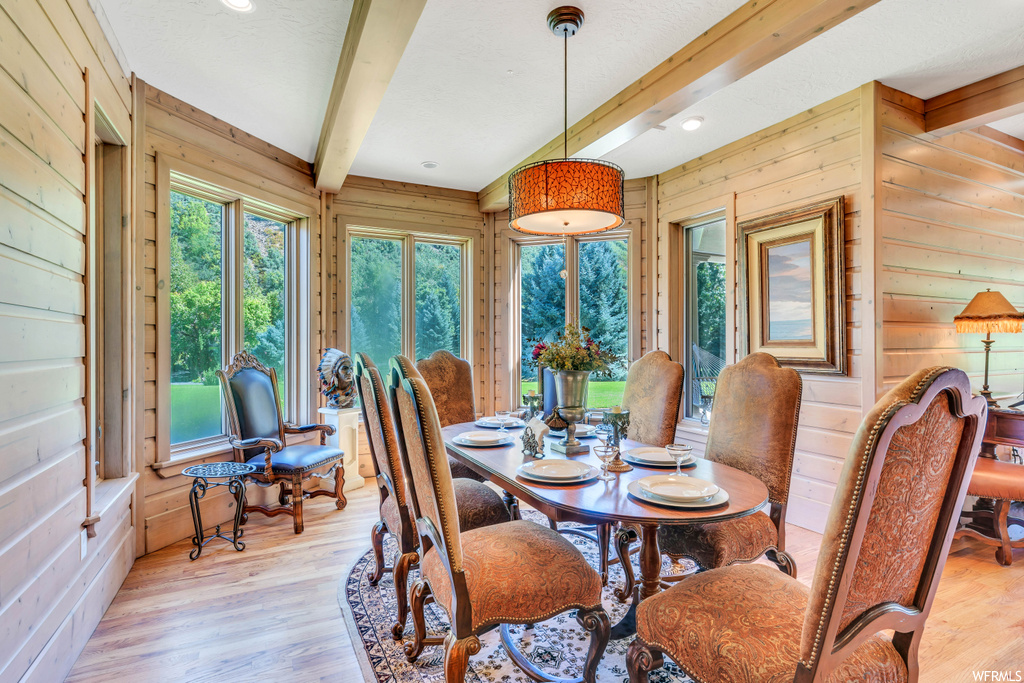 Dining space with beam ceiling, wooden walls, and light hardwood flooring