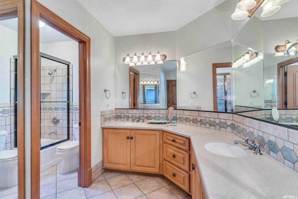 Full bathroom featuring tiled shower / bath combo, dual bowl vanity, tile floors, and toilet