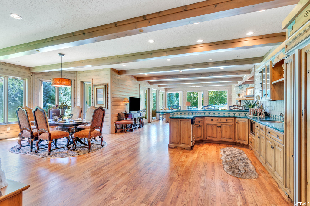 Kitchen featuring light hardwood floors, a healthy amount of sunlight, decorative light fixtures, and beamed ceiling