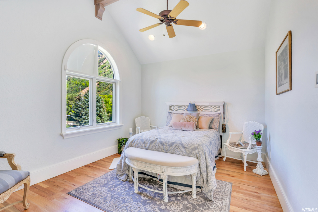 Hardwood floored bedroom with vaulted ceiling high, ceiling fan, and beamed ceiling