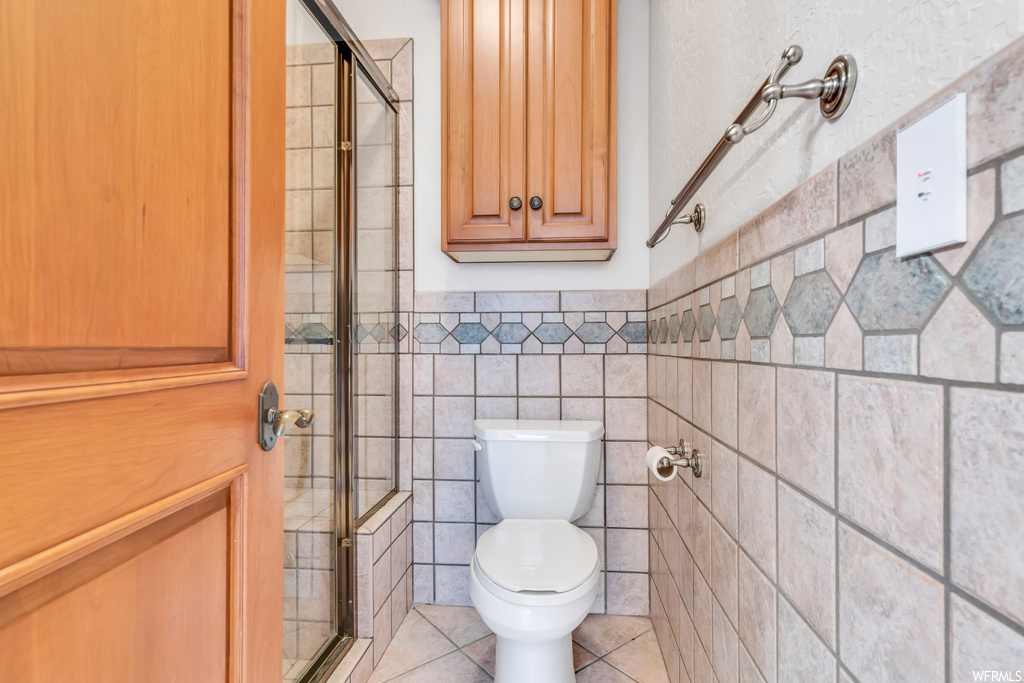 Bathroom featuring walk in shower, tile floors, toilet, and tile walls