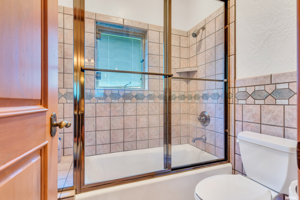 Bathroom with toilet, tile walls, and enclosed tub / shower combo