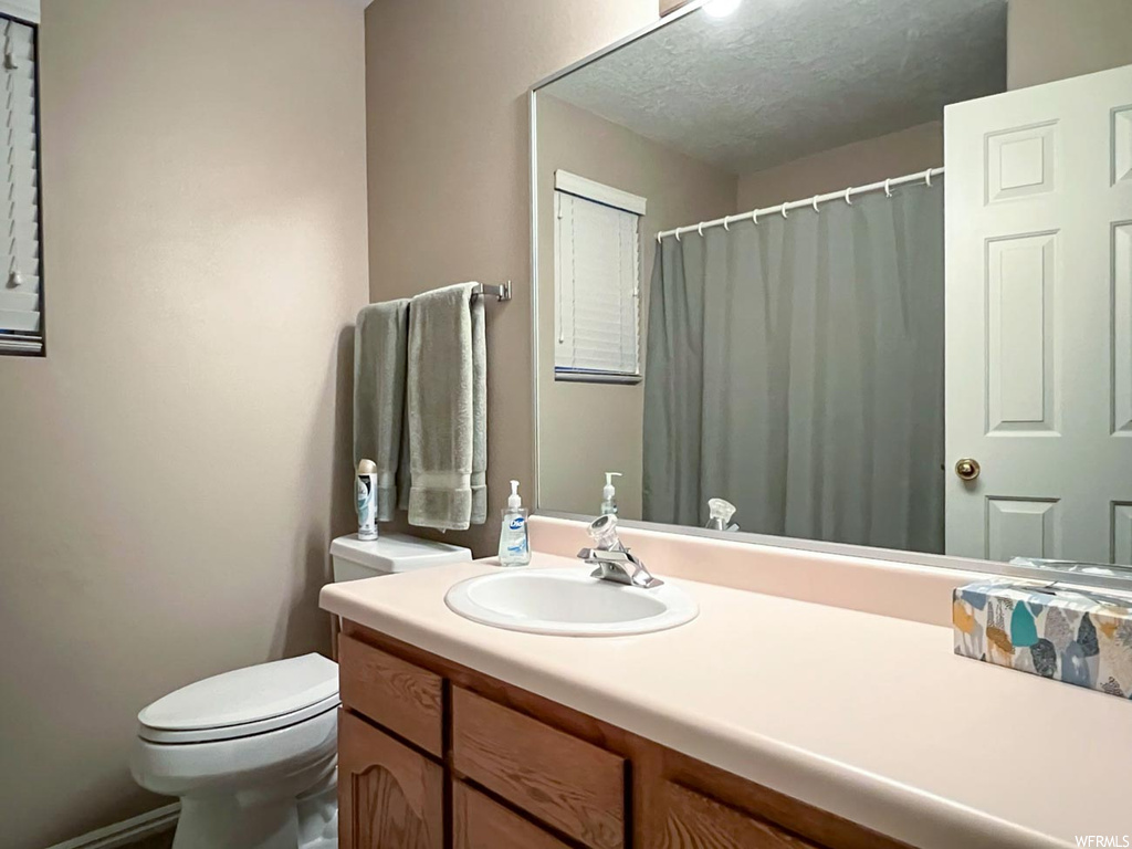 Bathroom with a textured ceiling, toilet, and vanity with extensive cabinet space