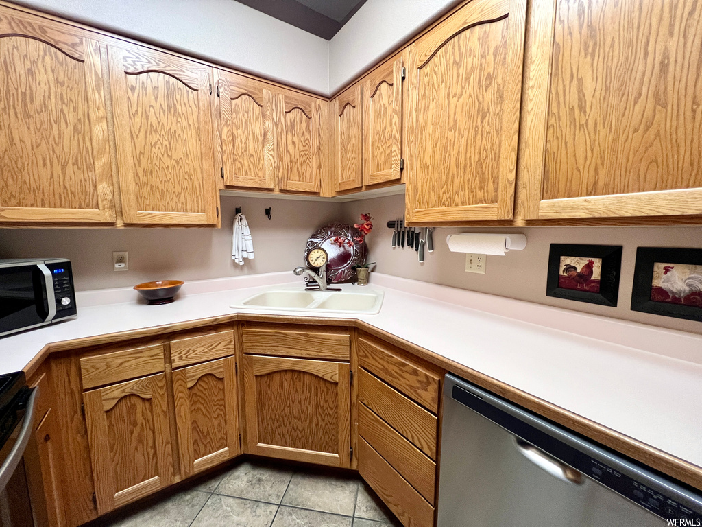 Kitchen with sink, light tile floors, stainless steel dishwasher, and range