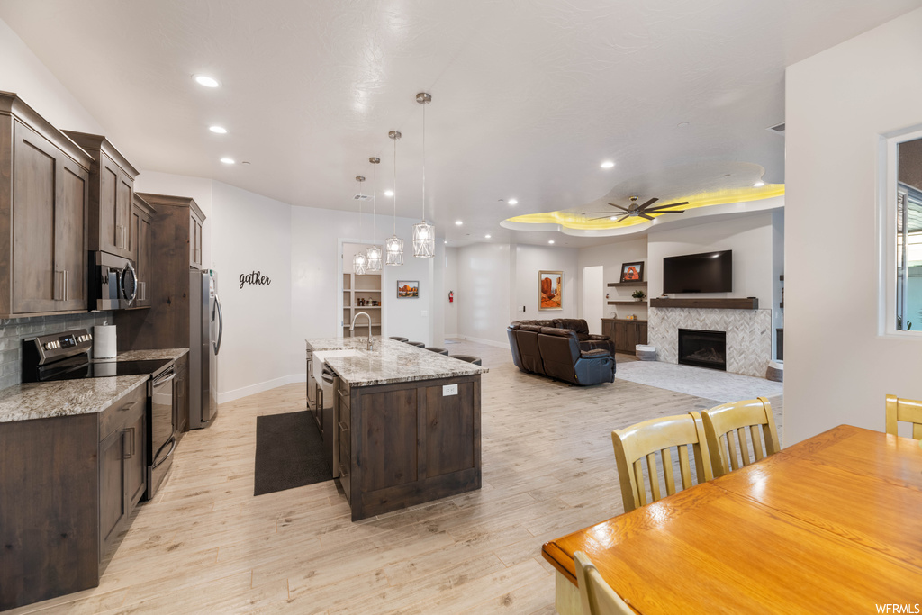 Kitchen with stainless steel appliances, light wood-type flooring, a center island with sink, and ceiling fan