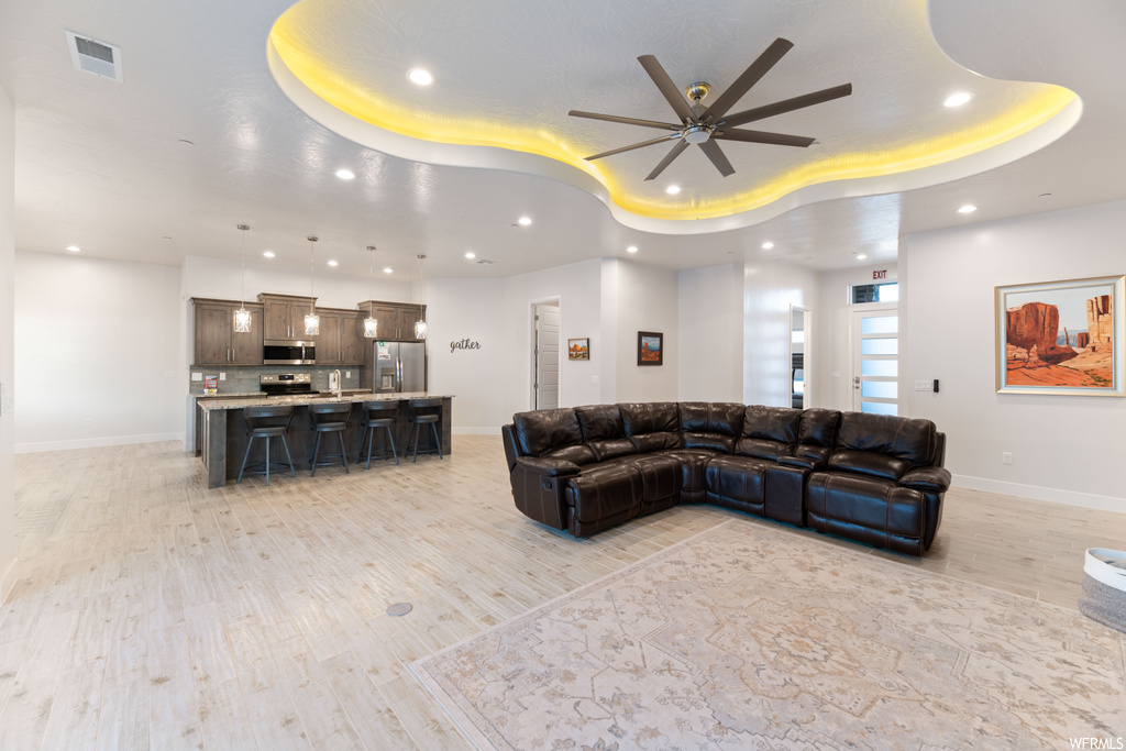 Living room featuring a tray ceiling, light hardwood / wood-style flooring, and ceiling fan