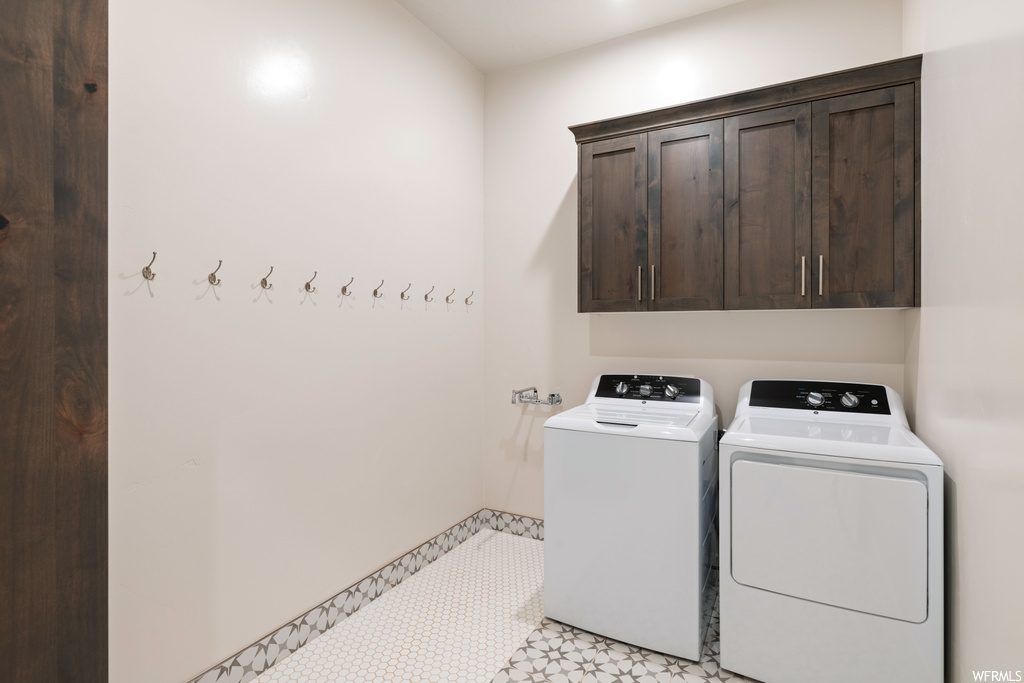 Clothes washing area with separate washer and dryer, cabinets, and light tile floors