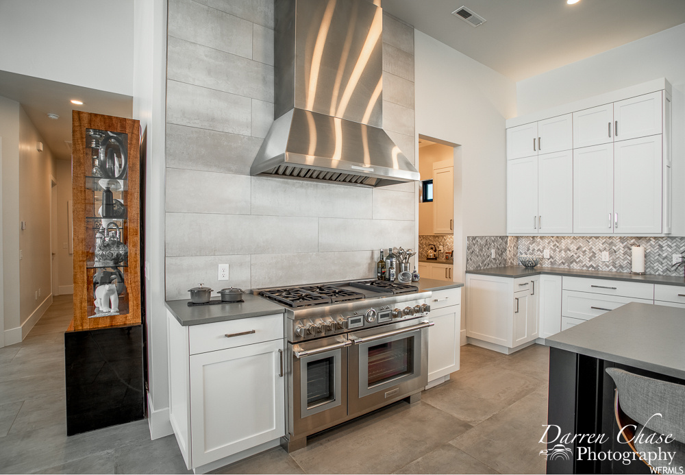 Kitchen featuring white cabinets, light tile floors, range with two ovens, tasteful backsplash, and wall chimney exhaust hood