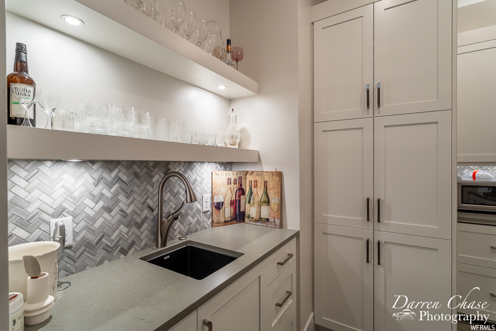 Kitchen featuring white cabinetry, tasteful backsplash, stainless steel microwave, and sink