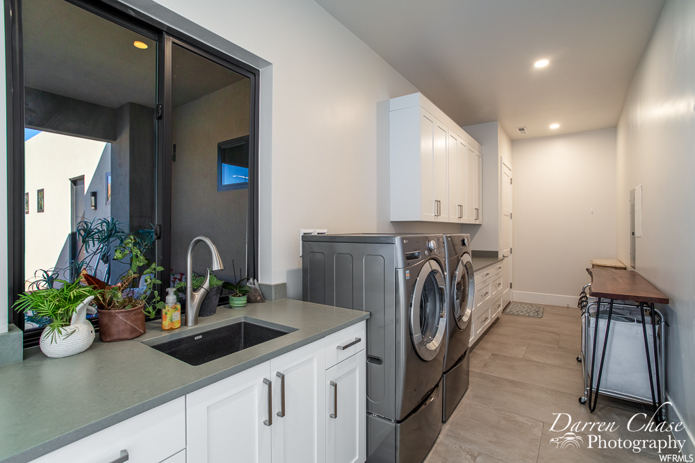 Laundry room with sink, washer and dryer, cabinets, and light hardwood floors