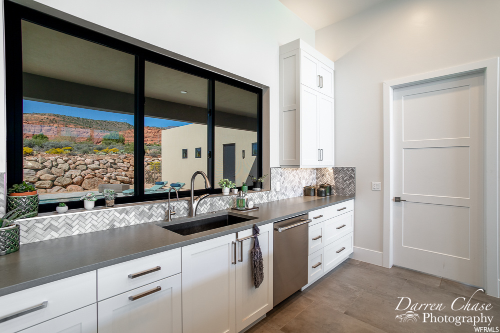 Kitchen featuring sink, white cabinets, backsplash, light tile flooring, and stainless steel dishwasher