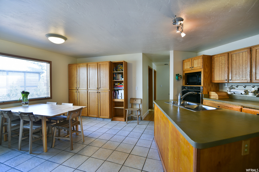 Kitchen with a center island with sink, black appliances, sink, and light tile floors
