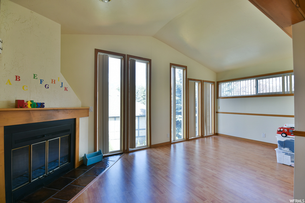 Unfurnished living room with a wealth of natural light, a fireplace, dark hardwood floors, and vaulted ceiling