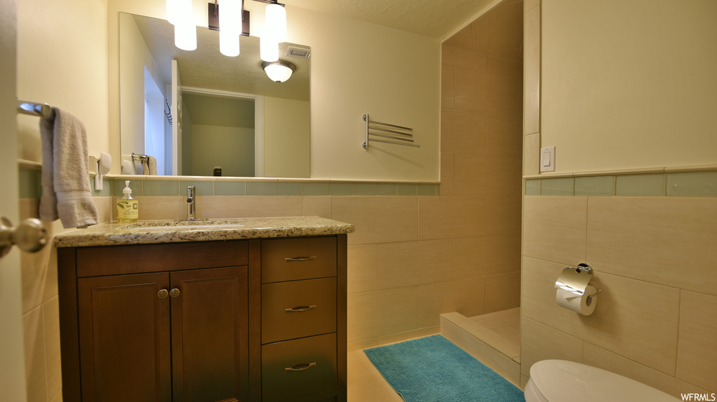 Bathroom with toilet, tasteful backsplash, tile walls, a textured ceiling, and vanity