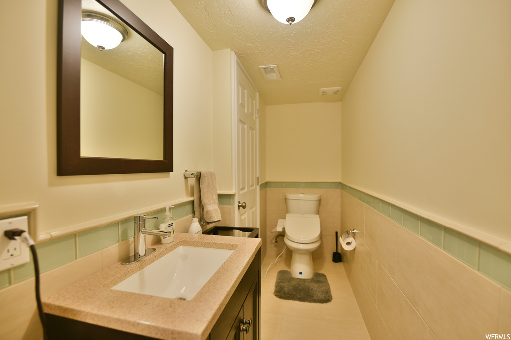 Bathroom featuring tile flooring, toilet, a textured ceiling, tile walls, and large vanity
