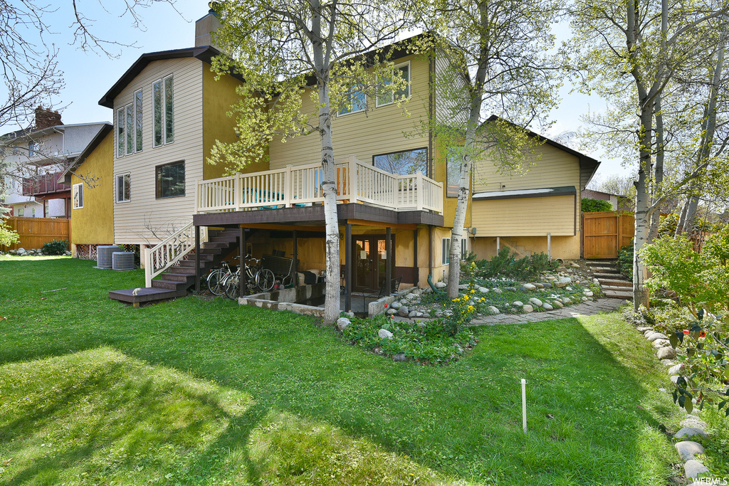 Rear view of property featuring central air condition unit, a lawn, and a deck