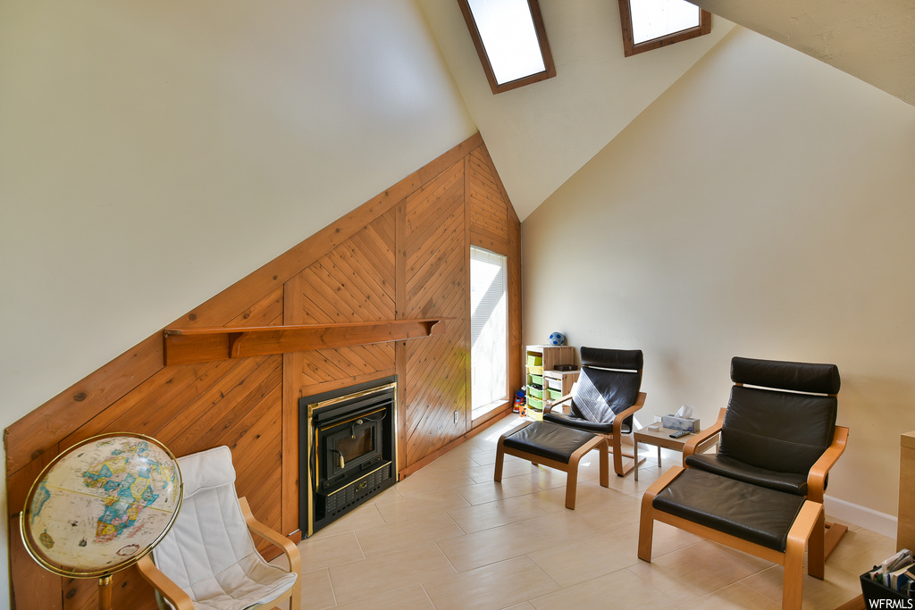 Tiled living room featuring wood walls, a fireplace, a skylight, and vaulted ceiling high