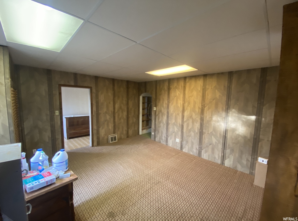 Misc room with light carpet, a paneled ceiling, and wooden walls