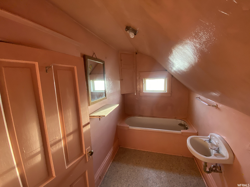 Bathroom featuring lofted ceiling, sink, and a bath to relax in