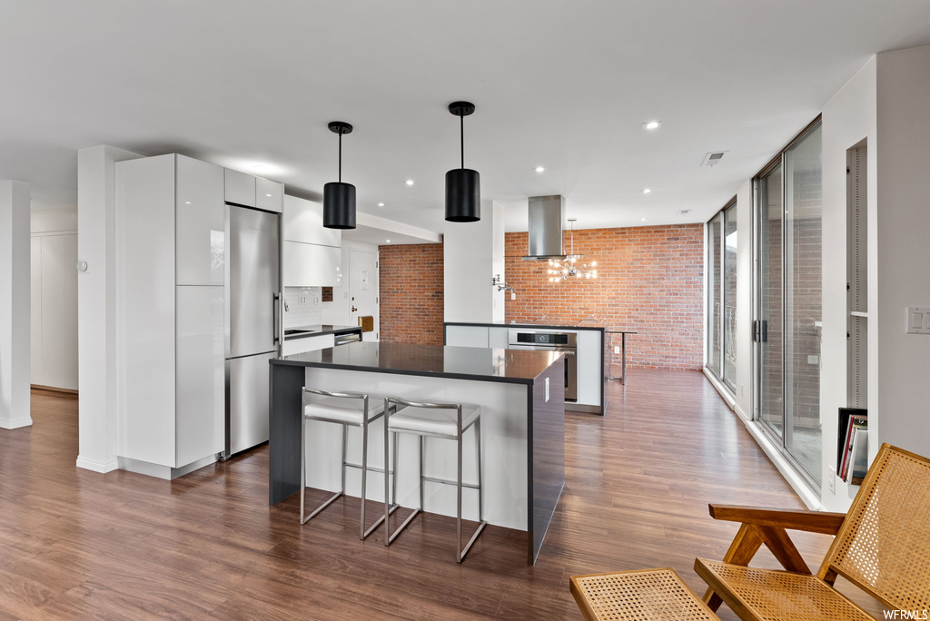 Kitchen featuring dark hardwood / wood-style flooring, pendant lighting, stainless steel appliances, wall chimney exhaust hood, and white cabinets
