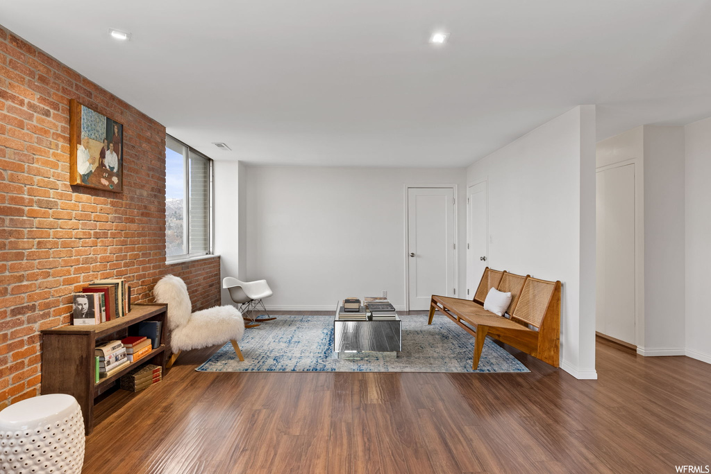 Living room with dark hardwood / wood-style flooring and brick wall