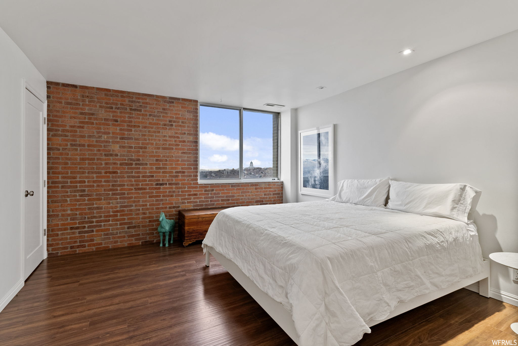 Bedroom with brick wall and dark hardwood / wood-style flooring