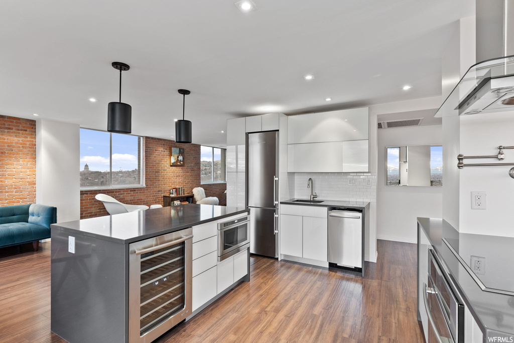 Kitchen with appliances with stainless steel finishes, dark wood-type flooring, beverage cooler, and white cabinetry