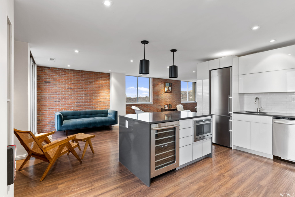 Kitchen featuring beverage cooler, light hardwood / wood-style floors, pendant lighting, appliances with stainless steel finishes, and white cabinetry