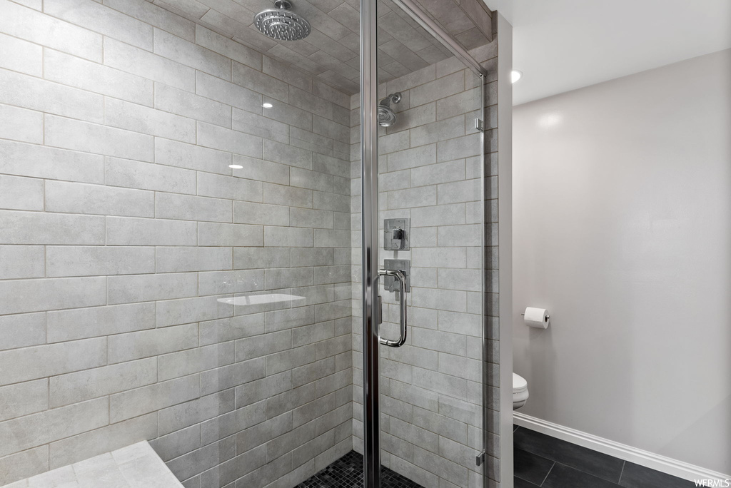 Bathroom with toilet, an enclosed shower, and tile flooring