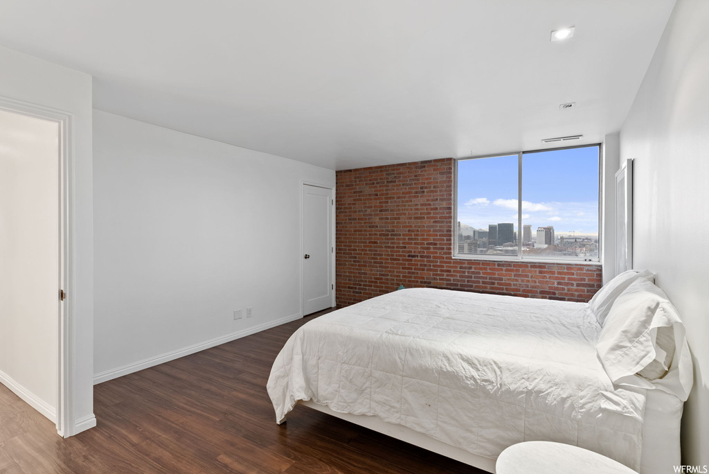 Bedroom featuring dark hardwood / wood-style flooring and brick wall